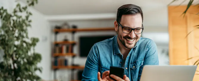 Portrait of a happy man with smart phone and laptop, indoors.