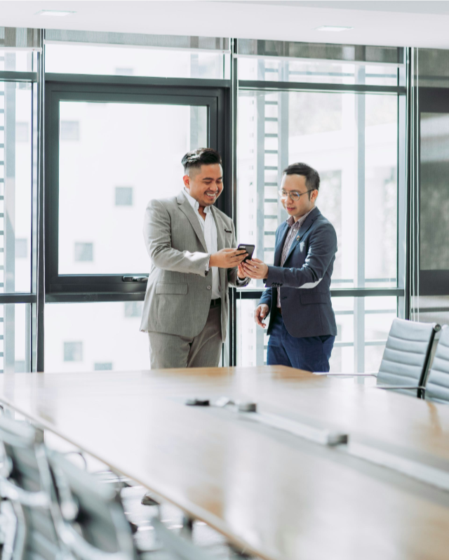 Two happy business men sharing message on phone in a bright office